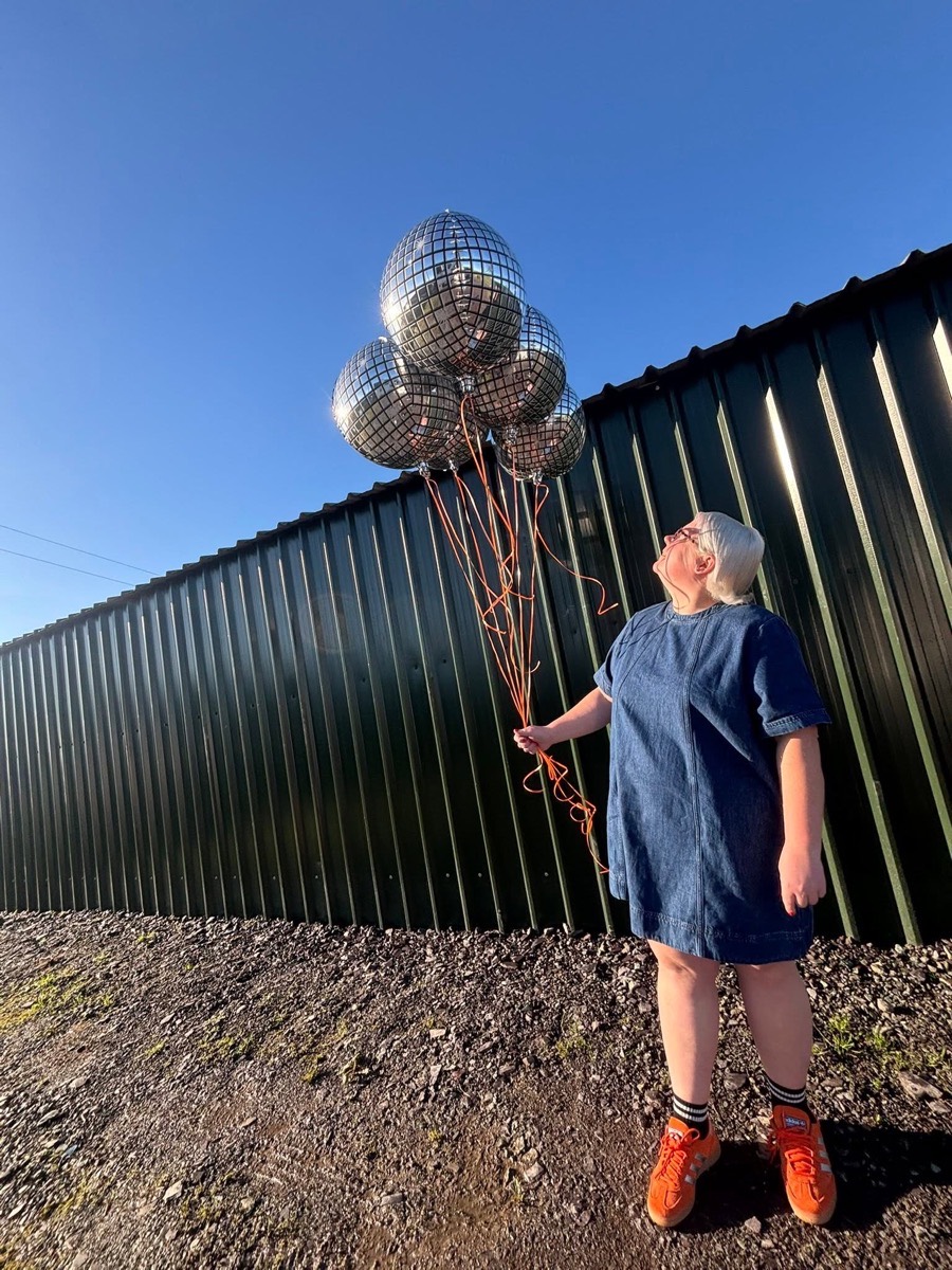 Amy outdoors on a sunny day, holding a bunch of disco ball balloons