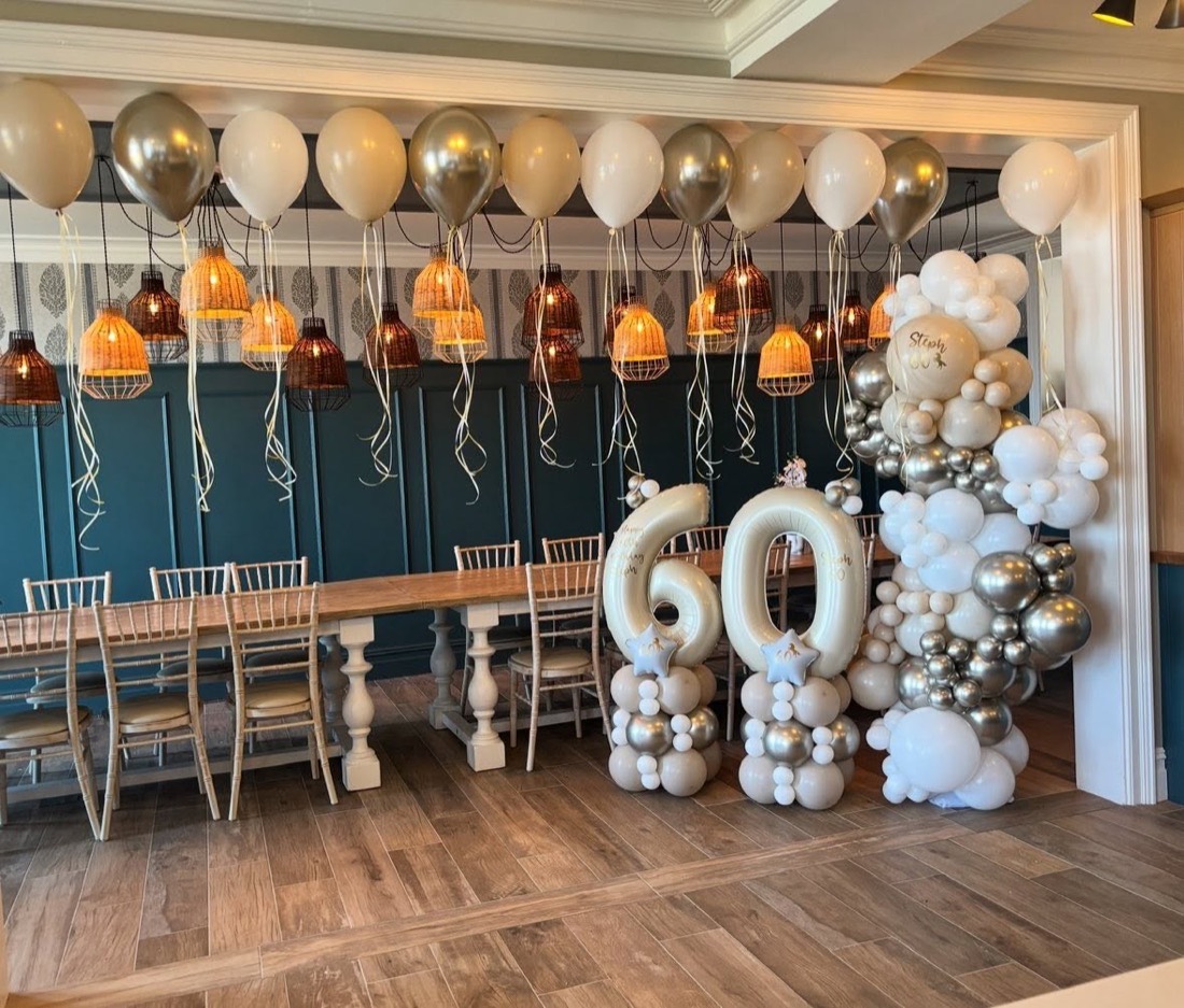 Gold and white 60th balloon display with a balloon ceiling over a long dinner table