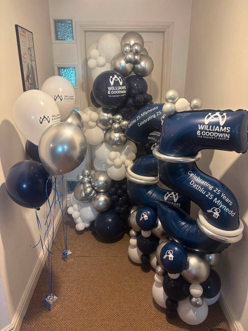 Navy, silver and white balloon columns printed with a company logo and a 25 years message in Welsh and English