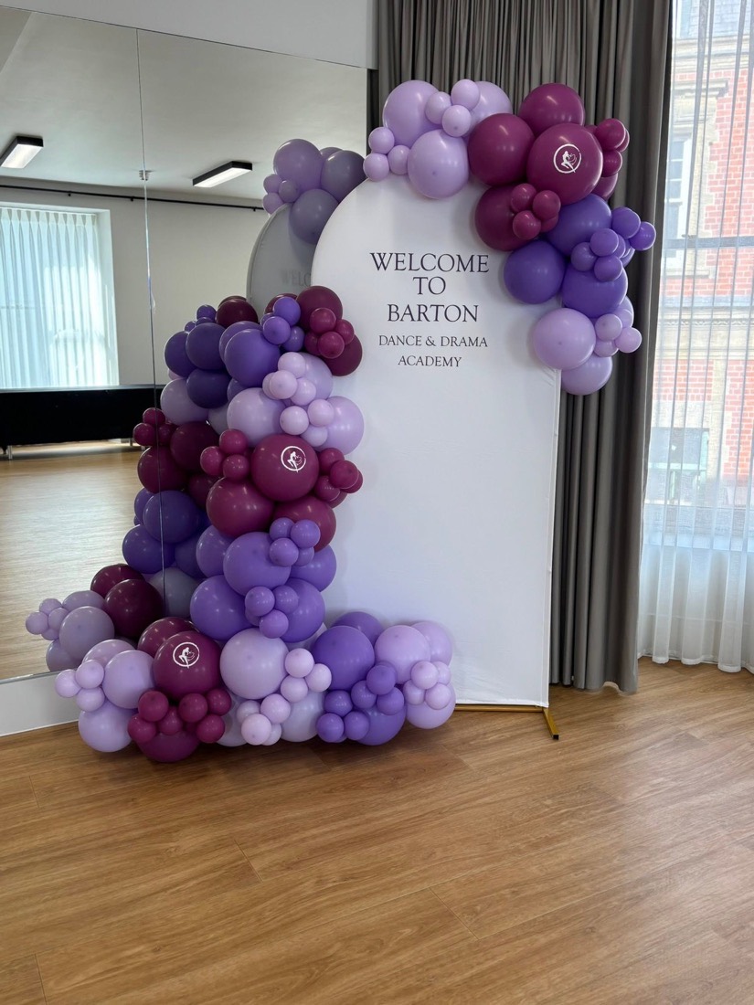 Purple and lilac balloon garland wrapped around an arched welcome sign